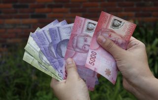 Mano sosteniendo billetes chilenos, representando el apoyo económico del Subsidio Único Familiar en San Bernardo.